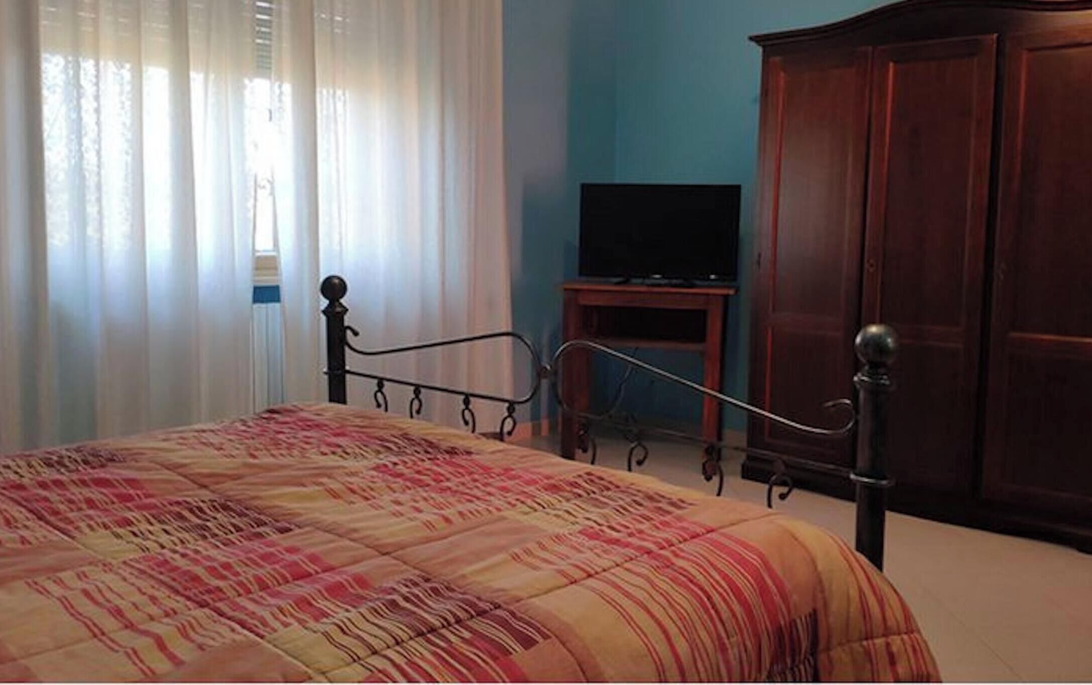 Un dormitorio con cama, cortinas, un televisor sobre un mueble bajo y un armario.