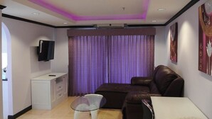 Una sala de estar moderna con un sofá de cuero marrón, un mueble blanco, una mesa de centro de vidrio y un televisor de pantalla plana montado en la pared.