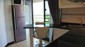 Cocina compacta con refrigerador, microondas y pileta. Hay un taburete cerca de una ventana con vistas.