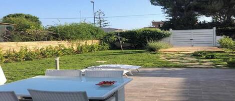 Un patio al aire libre con una mesa y sillas, un camino empedrado y un seto al fondo.