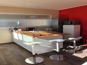 A modern kitchen with a wooden countertop, white bar stools, and a microwave on a cabinet.