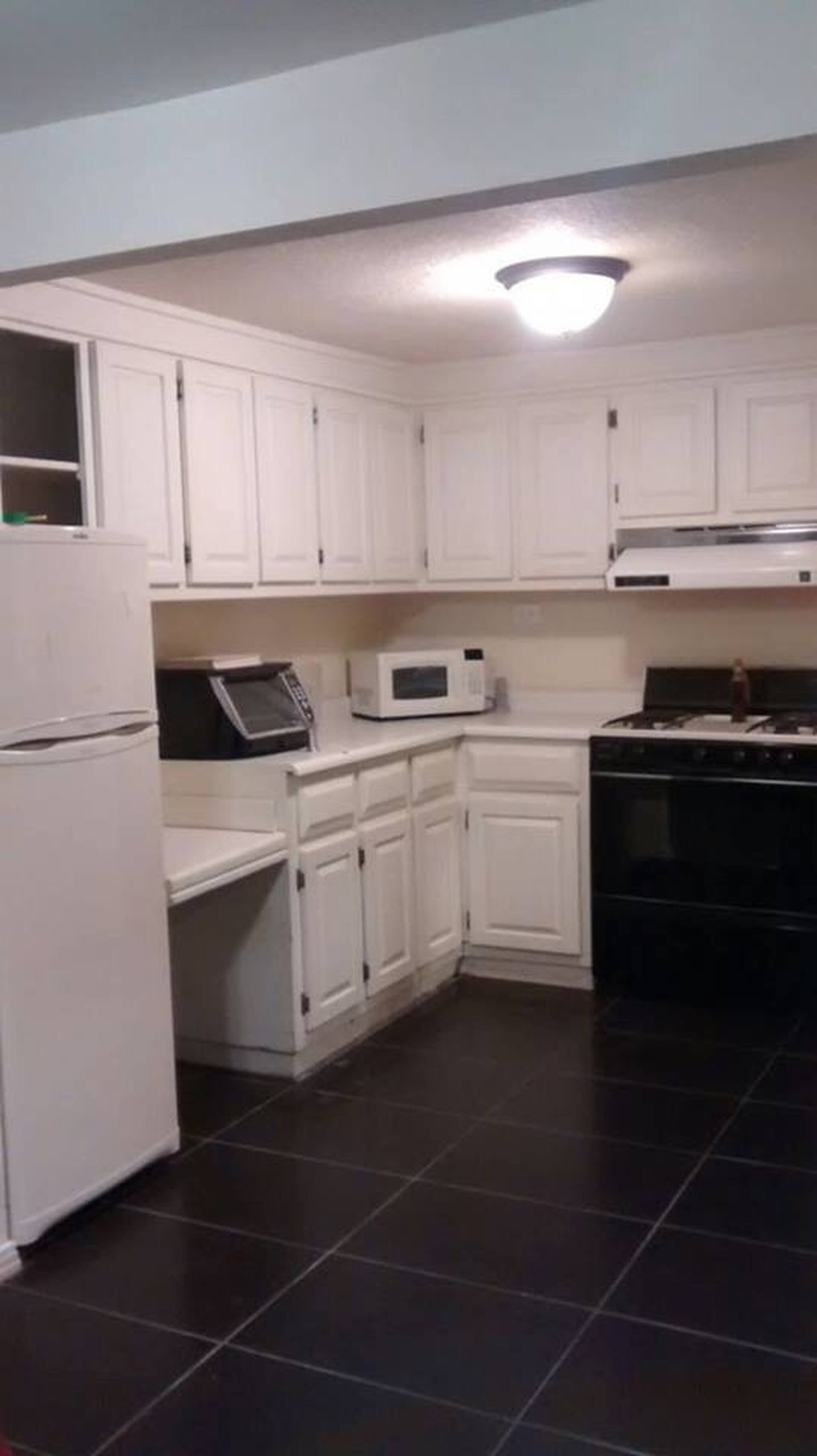 A kitchen with white cabinets, a microwave, a stove, and a refrigerator.