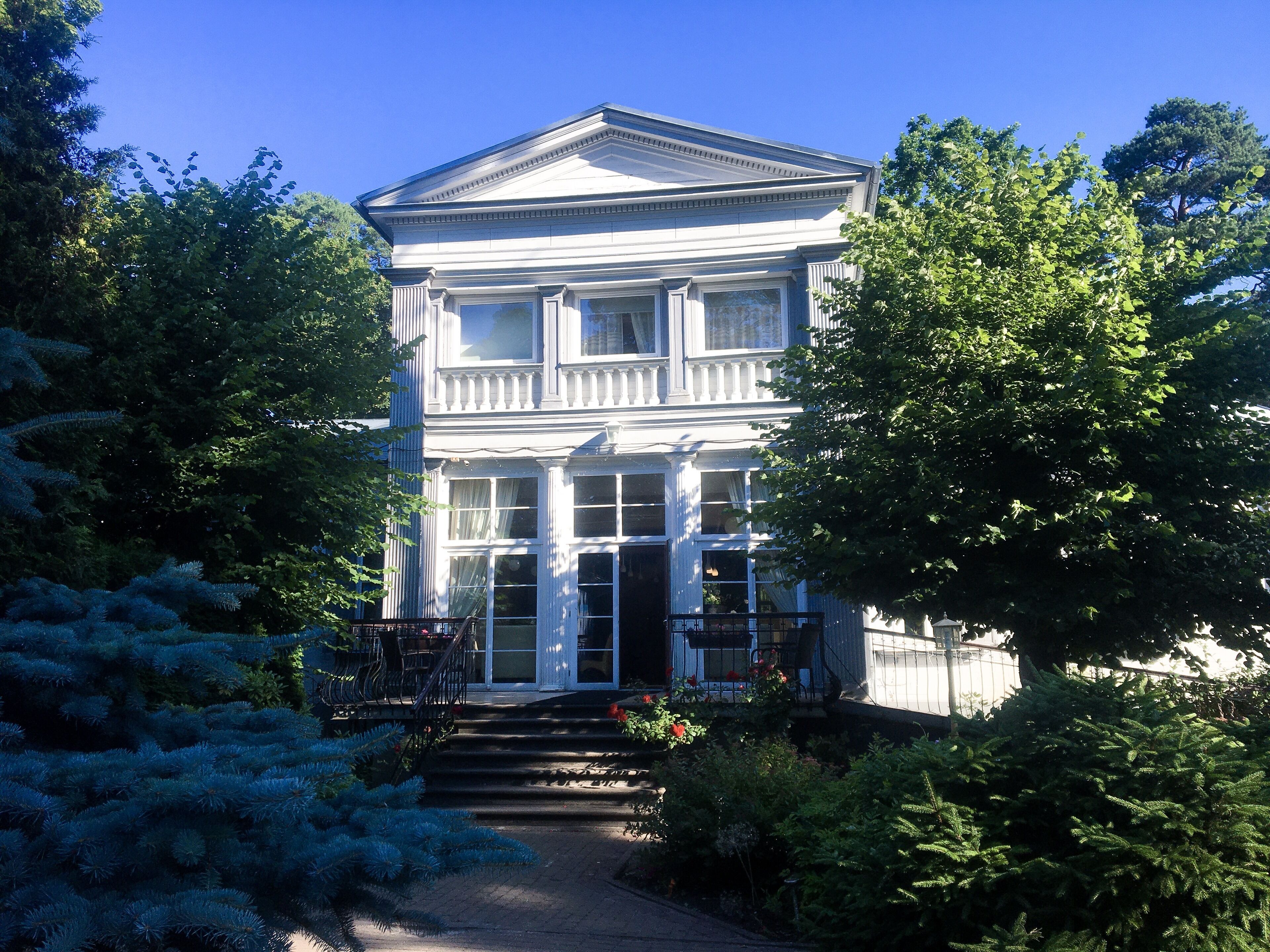 A two-story building with a symmetrical facade, large windows, and a central entrance with steps leading up to it.