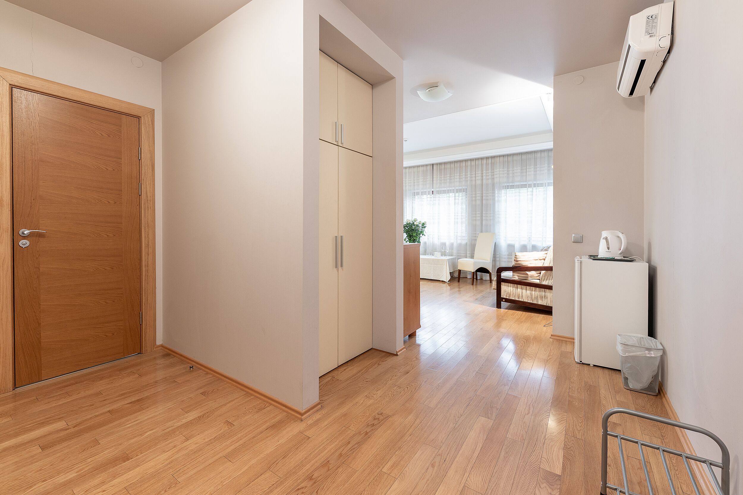 A hallway with wooden flooring, a wooden door, and a white wall with an air conditioning unit.