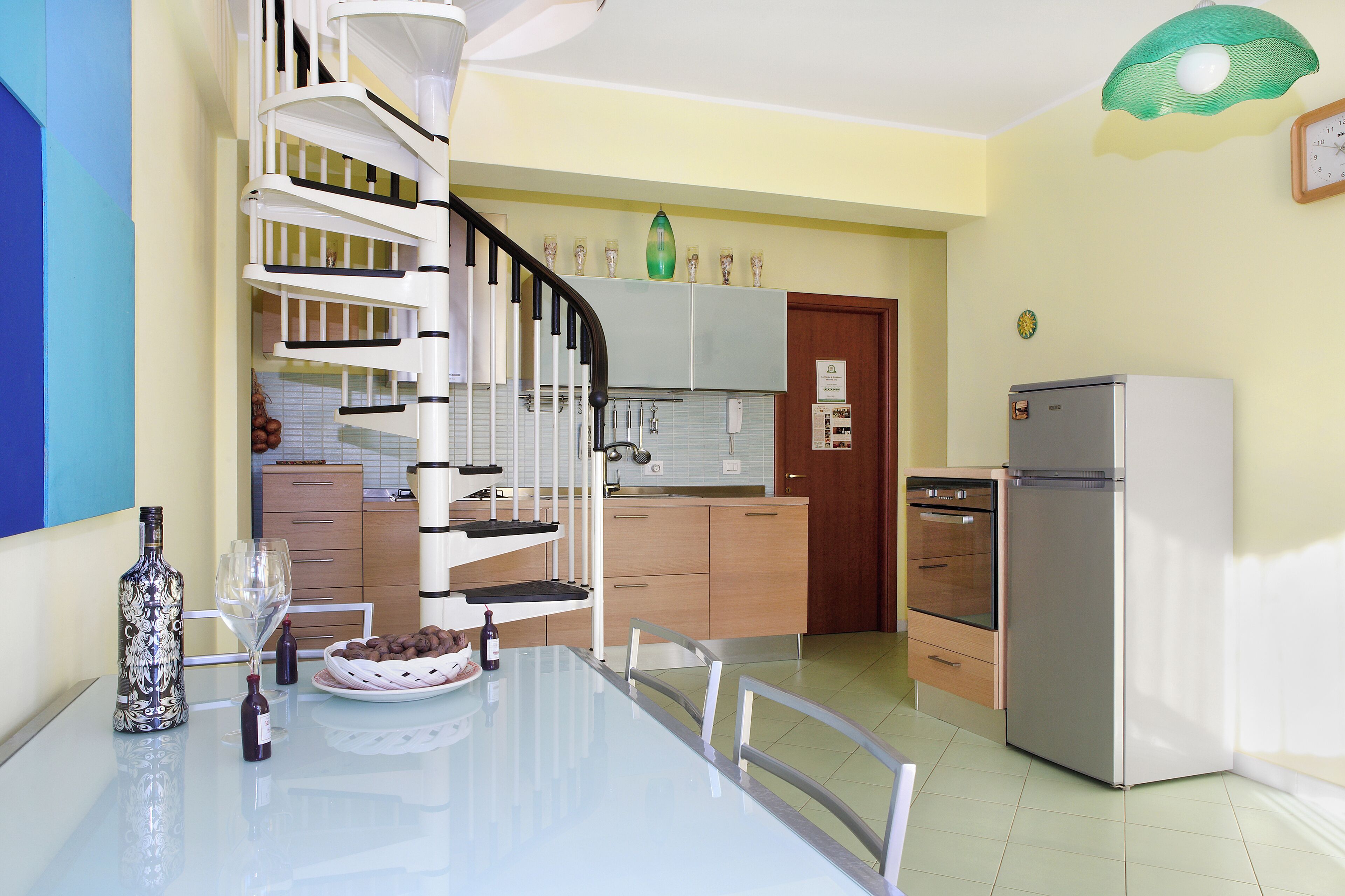 Eine moderne Küche mit Wendeltreppe, einem Esstisch mit Stühlen und einem Kühlschrank.