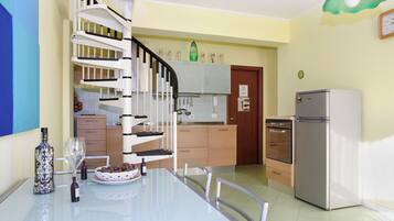 Eine moderne Küche mit Wendeltreppe, einem Esstisch mit Stühlen und einem Kühlschrank.