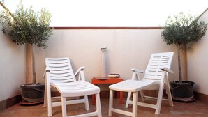 Deux chaises en plastique blanc et une petite table, le tout placé dans un espace extérieur carrelé agrémenté de plantes en pot.