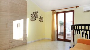 Une chambre avec une armoire en bois, une porte-fenêtre coulissante donnant sur un balcon et une rambarde noire.