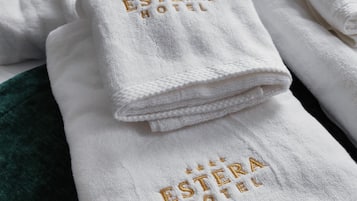 Toallas blancas dobladas con el logotipo 'ESTERA HOTEL' bordado en dorado, sobre un edredón verde.