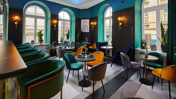 A modern interior with teal walls, arched windows, and a variety of seating arrangements including green and orange chairs. - Hotel Estera (Kraków)