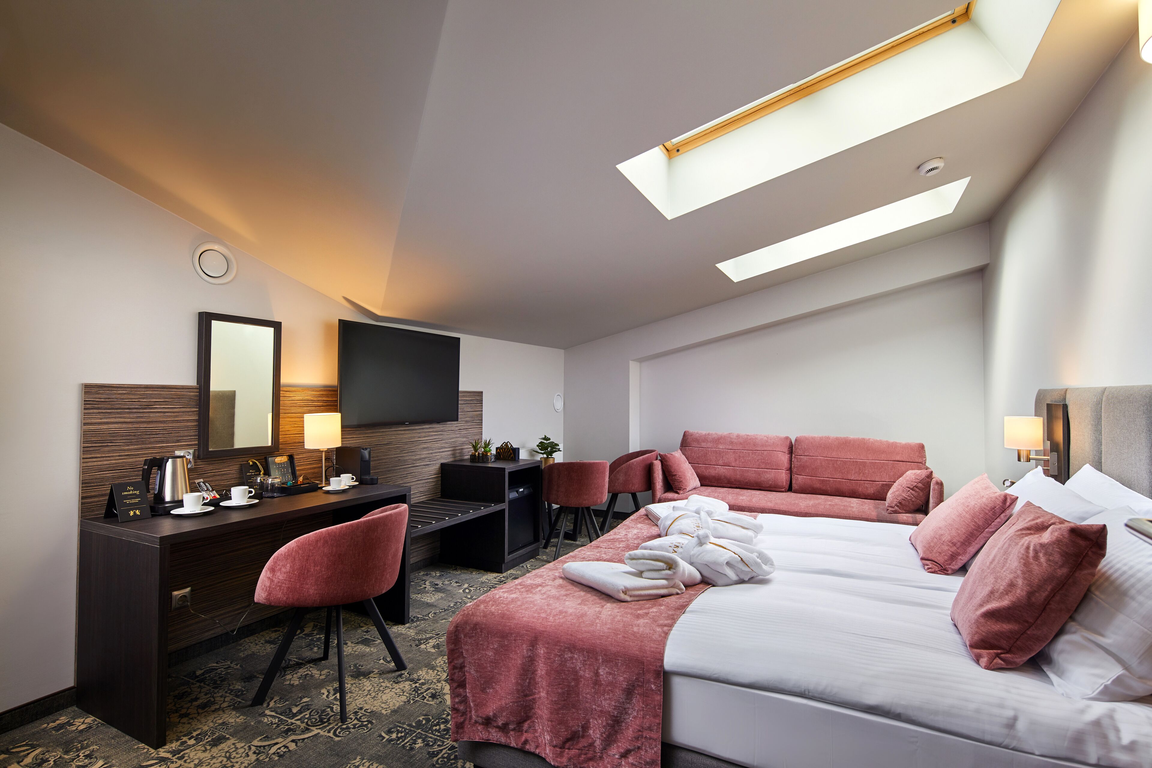 Una camera d'albergo con un letto, una scrivania, una televisione e una finestra con lucernario.