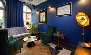 A room with a blue wall, a tufted sofa, green armchairs, a round coffee table, and a floor lamp. - Hotel Estera (Kraków)