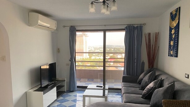 A living room with a sofa, a TV, a small table, and a balcony with curtains. - Angket Hip Residence in Jomtien Angket Floor 15 Room (Pattaya)