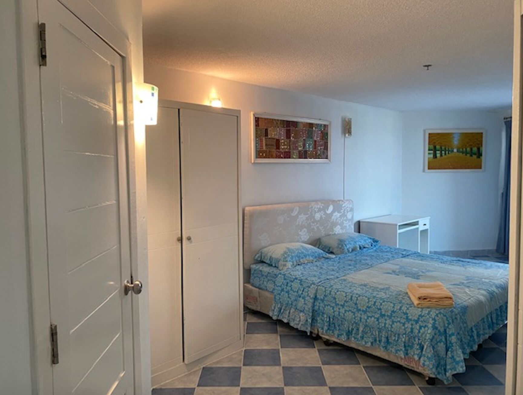 A bedroom with a bed, a nightstand, a door, and a wall with a painting.