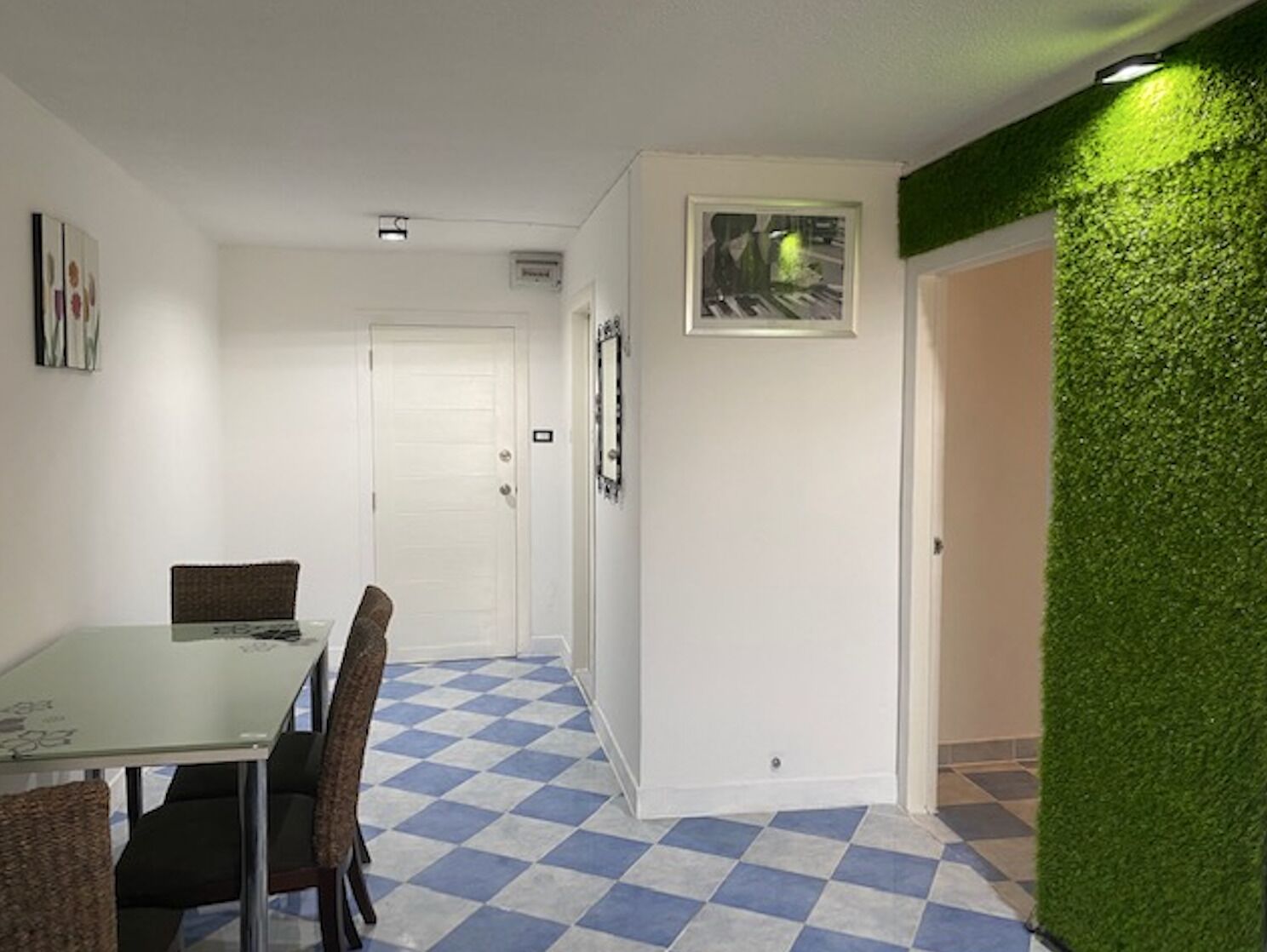 A room with a checkered floor, a dining table with chairs, a white door, and a green wall.