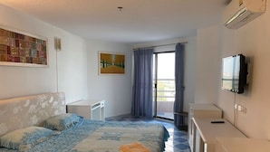 A hotel room with a bed, a desk, a chair, a TV, and a balcony with curtains. - Angket Hip Residence in Jomtien Angket Floor 15 Room (Pattaya)