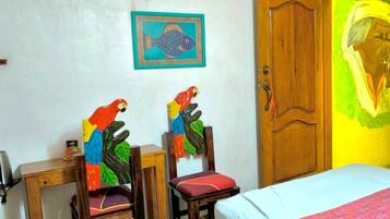 A room with a bed, two chairs, a wooden door, and a ceiling fan.
