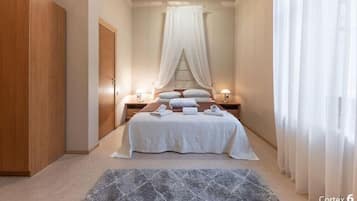A bedroom with a bed, two bedside tables, a nightstand, a wardrobe, and a curtain.