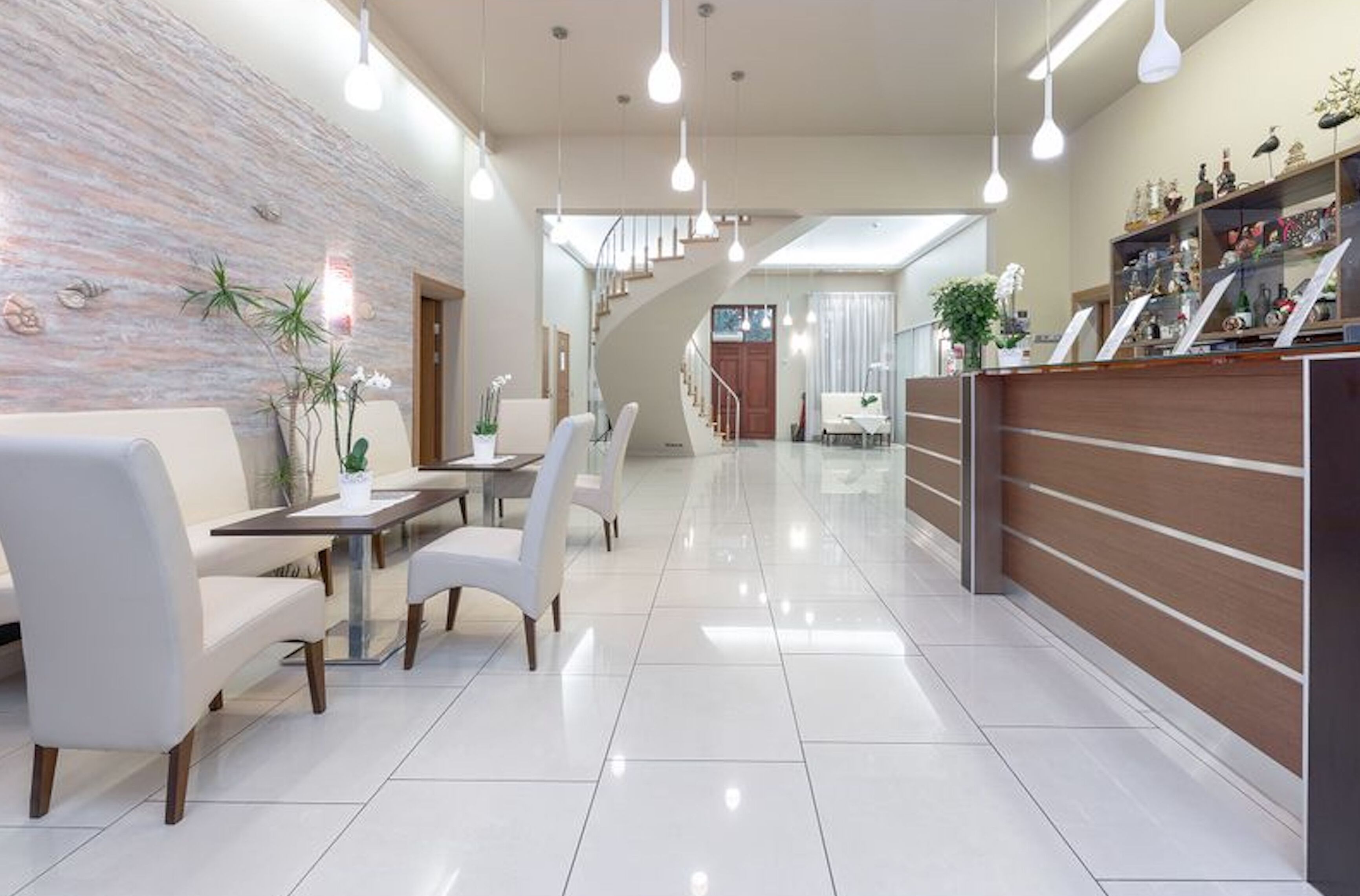 A modern hotel lobby with a reception desk, seating area, and a staircase leading to upper floors.