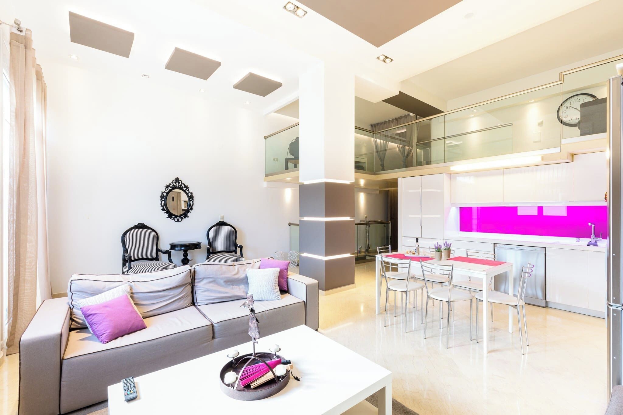 Un espacio moderno con sala de estar que incluye un sofá, sillas, una mesa de comedor y una cocina con un salpicadero de color rosa brillante.