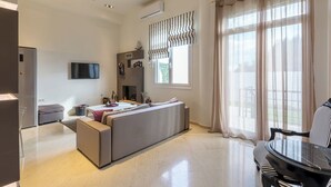 A modern living room with a sofa, a dining table, and a TV. - Gouves Beach Boutique Apartment (Hersonissos)
