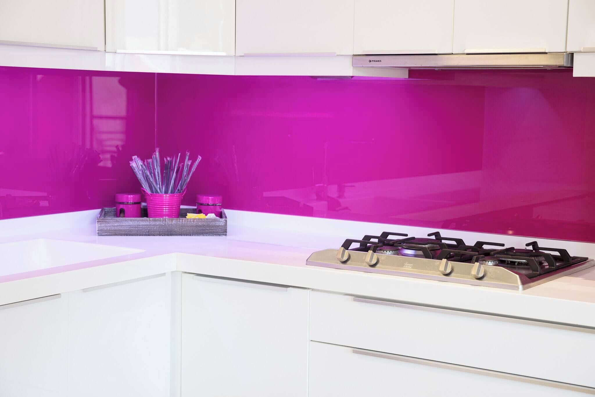 A kitchen with white cabinets, a gas stove, and a pink backsplash.