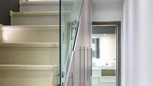 A modern staircase with glass railings leading to a bathroom with a sink and cabinets. - Gouves Beach Boutique Apartment (Hersonissos)