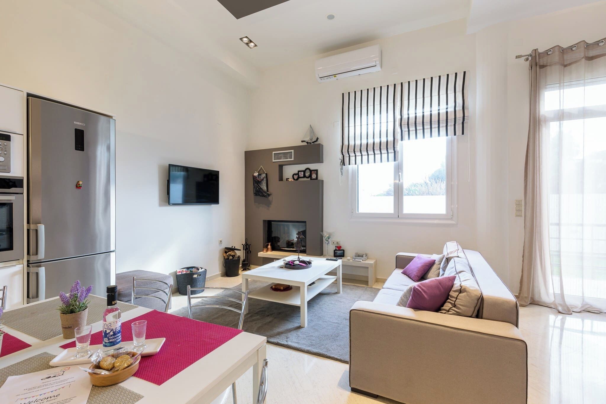 A modern living room with a sofa, a dining table, a TV, and a kitchen area with a refrigerator.