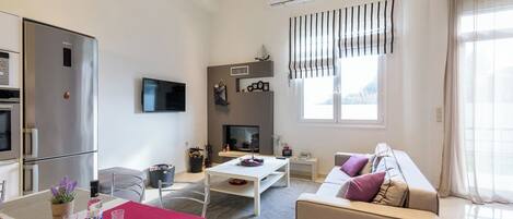A modern living room with a sofa, a dining table, a TV, and a kitchen area with a refrigerator.