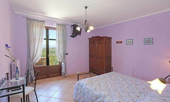 Ein Schlafzimmer mit einem Bett, einem Holzschrank, einem Tisch mit Stühlen, einem Fenster mit Vorhängen und einer Chandelier.