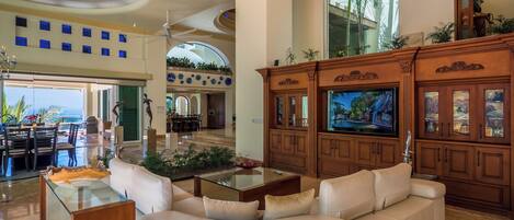 A spacious living area with a large TV, a white sofa, and a glass coffee table.