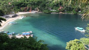 A coastal area with boats docked near a sandy beach, surrounded by lush greenery and buildings. - Fully Staffed, Beach Frontage Luxury Villa (Puerto Vallarta)