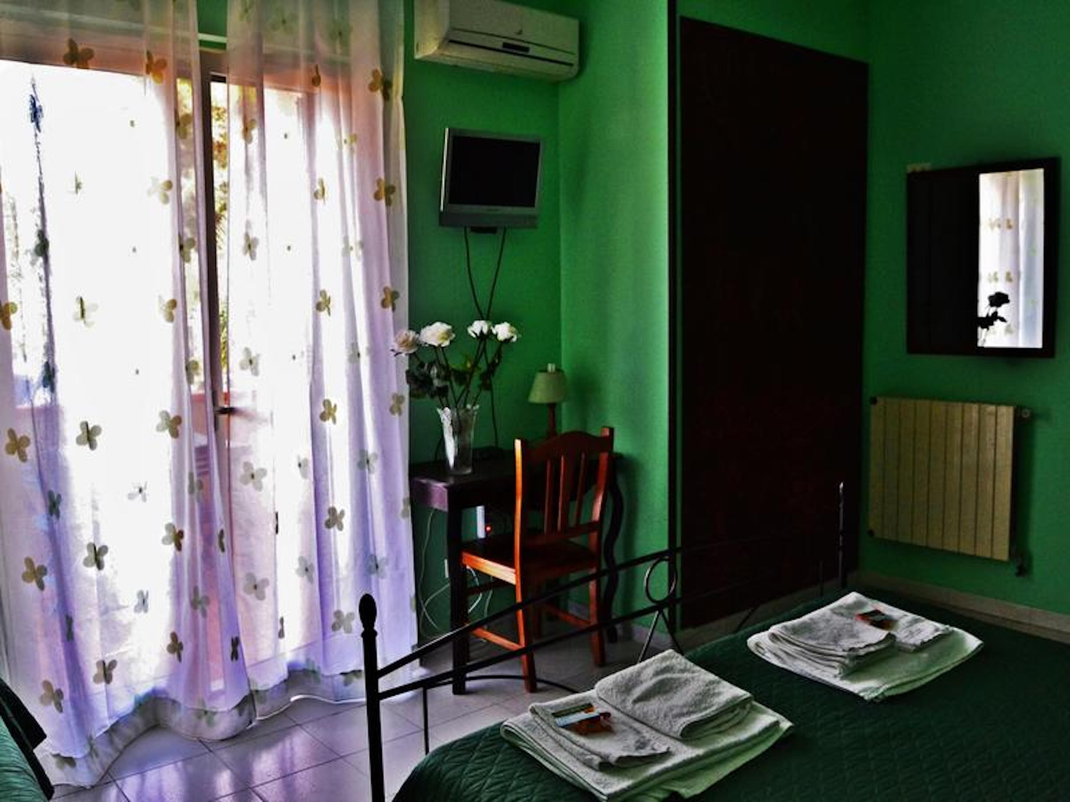 Une chambre avec un lit, un bureau et une chaise, une télévision et une fenêtre avec des rideaux.
