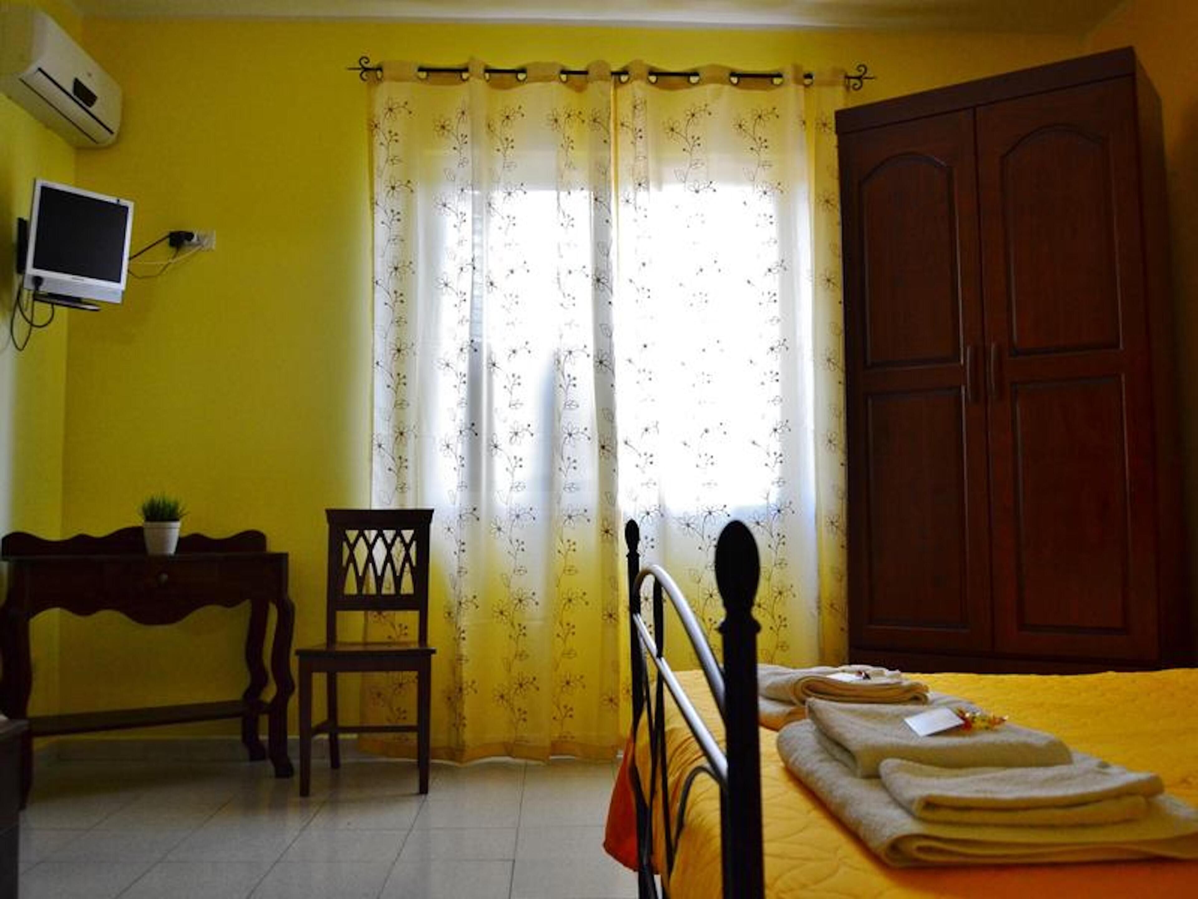 Una camera da letto con un letto, un'armadio in legno, una scrivania con una sedia e un televisore appeso al muro.