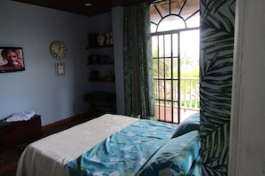 A room with a bed, a clock, a TV, and a window with curtains.