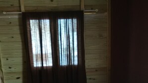 Ein Zimmer mit einem Bett, einem Fenster mit Vorhängen und einer Holzwand.