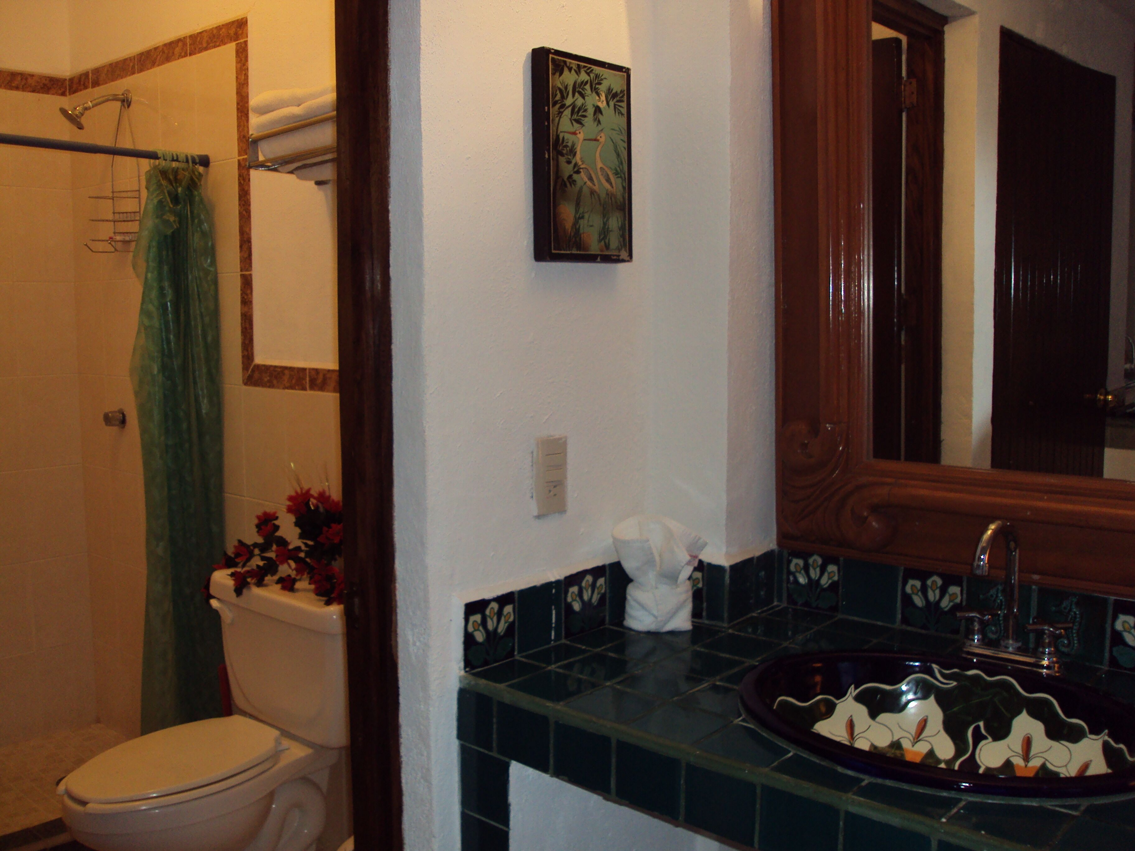Un baño con inodoro, ducha, lavamanos con recipiente decorativo y espejo.