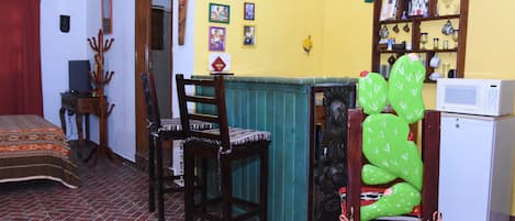 A room with a bed, a wooden chair, a green cushioned chair, a small table, a bookshelf, and a microwave.