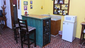 Une cuisine compacte avec un petit îlot central, des chaises en bois, un four à micro-ondes et une étagère contenant des ustensiles de cuisine.