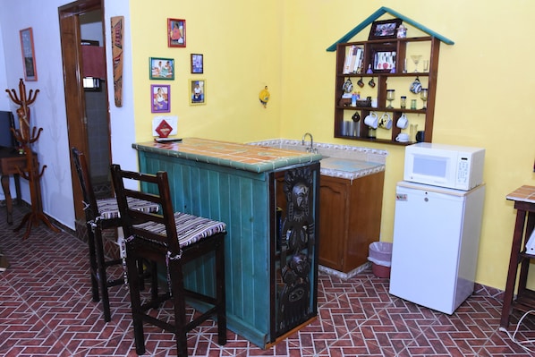 A compact kitchen with a small island, wooden chairs, a microwave, and a shelf with kitchenware. - Room-cancun Guest House 2 (Cancun)