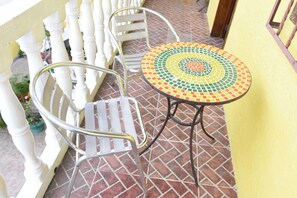 Un balcon dotĂ© dâun sol carrelĂ©, dâune chaise en mĂ©tal, dâune petite table ronde ornĂ©e dâun motif en mosaĂŻque et dâune rambarde blanche.
