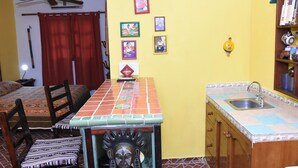 Une cuisine compacte dotée d’un plan de travail carrelé, d’un évier et d’un coin repas avec des chaises et une table.