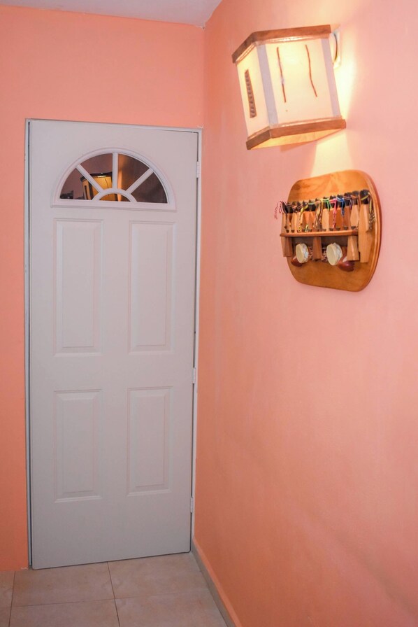 Un couloir avec une porte blanche, un luminaire fixé au mur et une étagère en bois sur laquelle sont disposés divers objets.