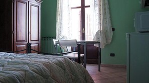 A bedroom with a bed, a chair, a desk, a radiator, and a window with curtains.
