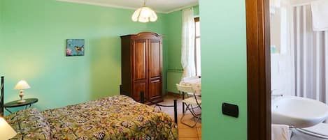 A room with a bed, a wooden cabinet, a table with a lamp, and a bathroom with a sink and toilet.