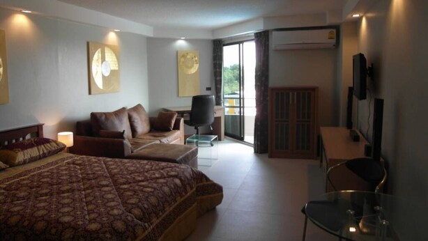 Un dormitorio moderno con una cama grande, un escritorio y una silla. Hay un televisor montado en la pared y una ventana con cortinas.