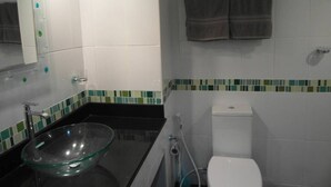 Un baño con un lavabo de vidrio, inodoro blanco y espejo con marco iluminado.