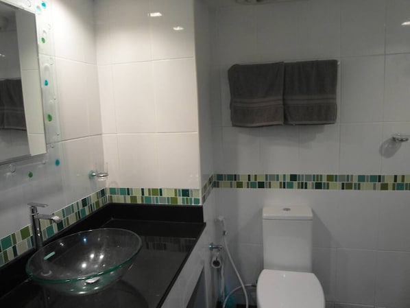 A bathroom with a glass sink, white toilet, and a mirror with a lighted frame.