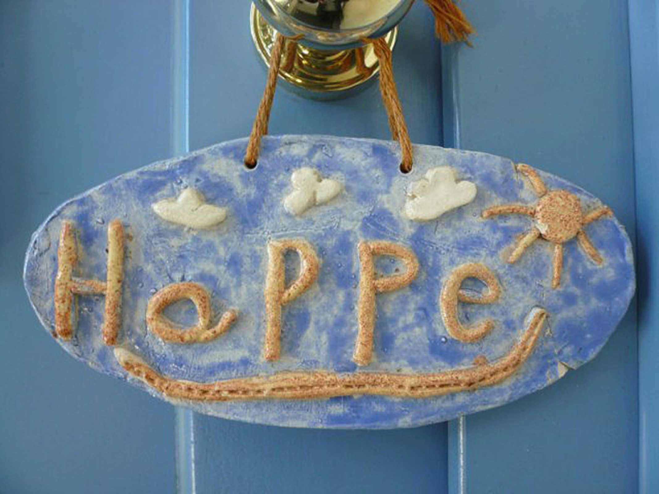Een blauw bord met de tekst 'Hepp' en een zon, hangend aan een blauwe deur.