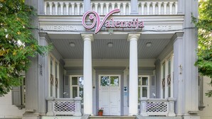Un hôtel de luxe à la façade classique, orné d’une inscription indiquant l’année de sa construction, et doté d’une entrée accueillante avec des marches et des plantes en pot.